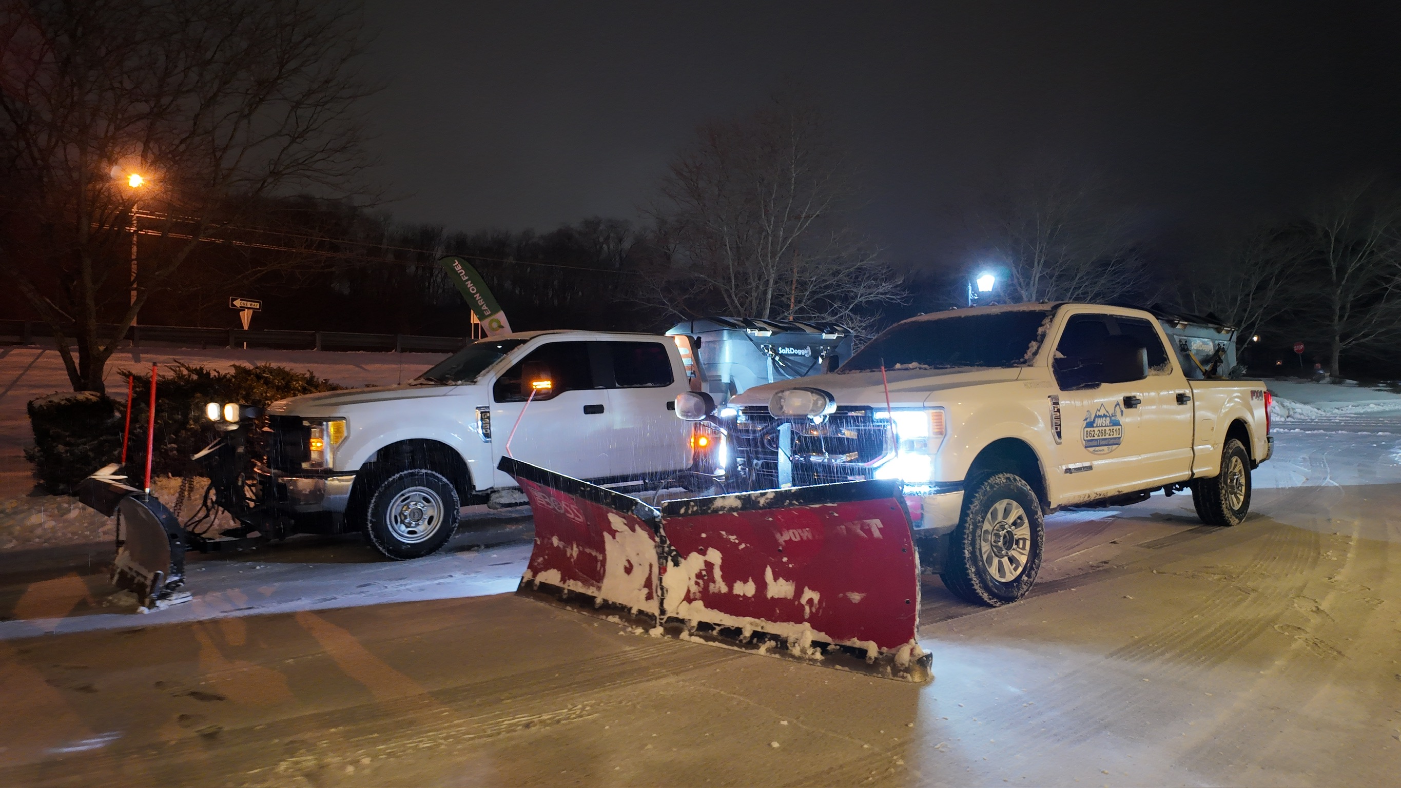 Multiple JRW Services plow trucks staged and working a lit commercial parking lot at night