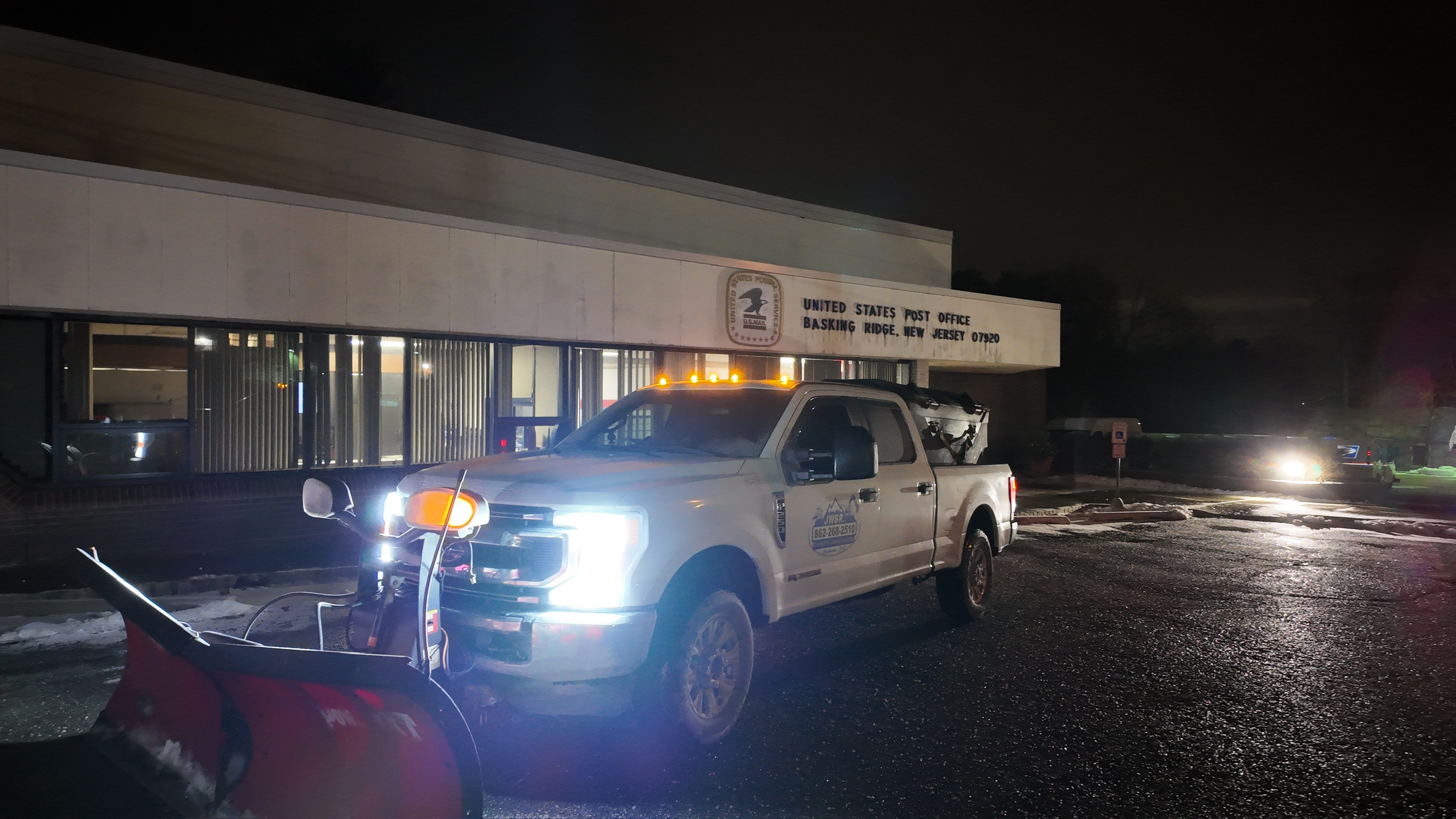 JRW Services plow truck clearing the lot at a US Post Office at night