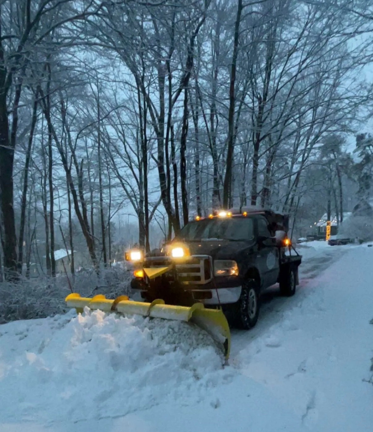 JRW Services plow truck clearing a wooded residential road at dusk