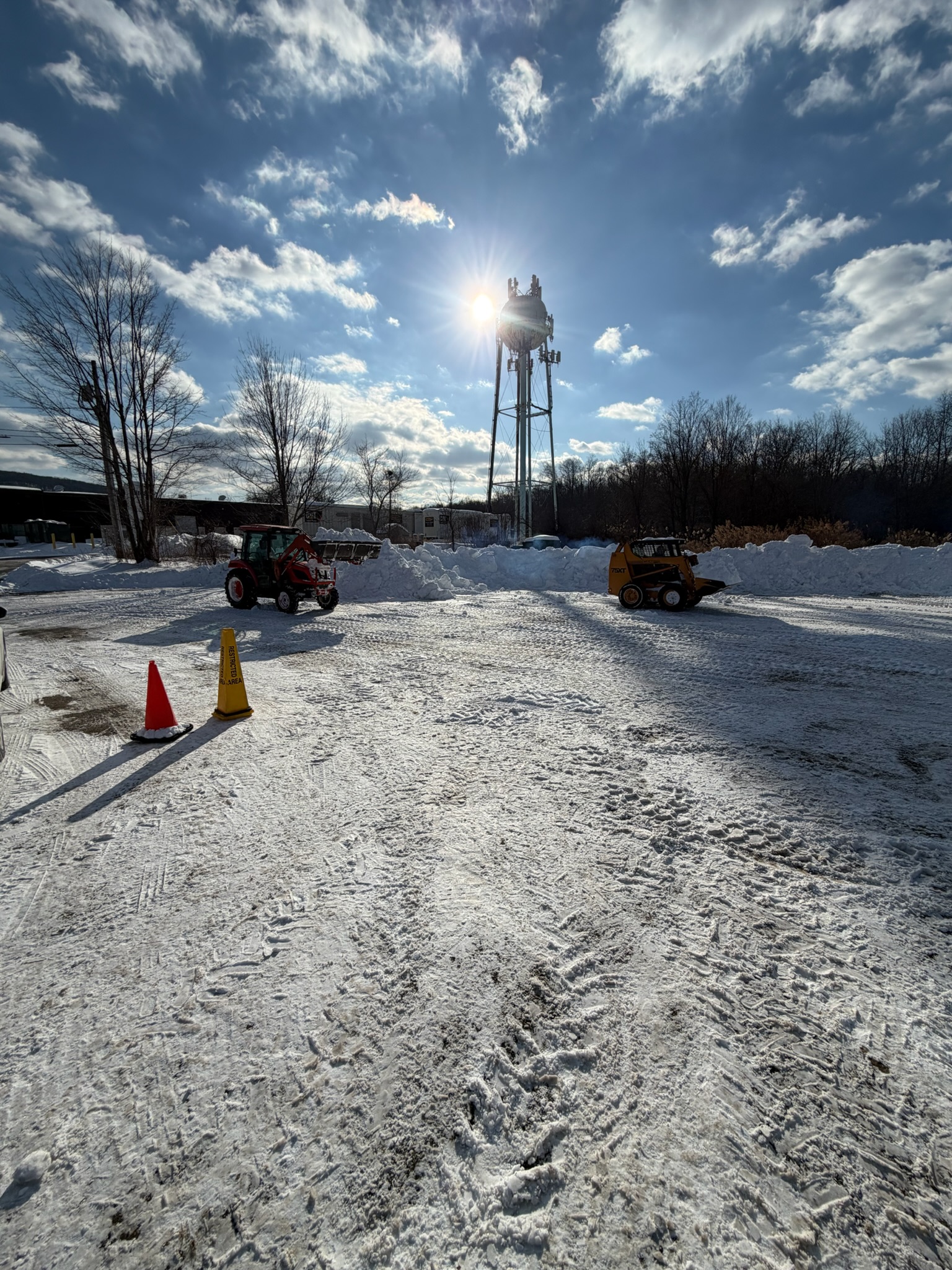 A tractor and a skid steer working the same commercial lot in daylight with safety cones marking the area