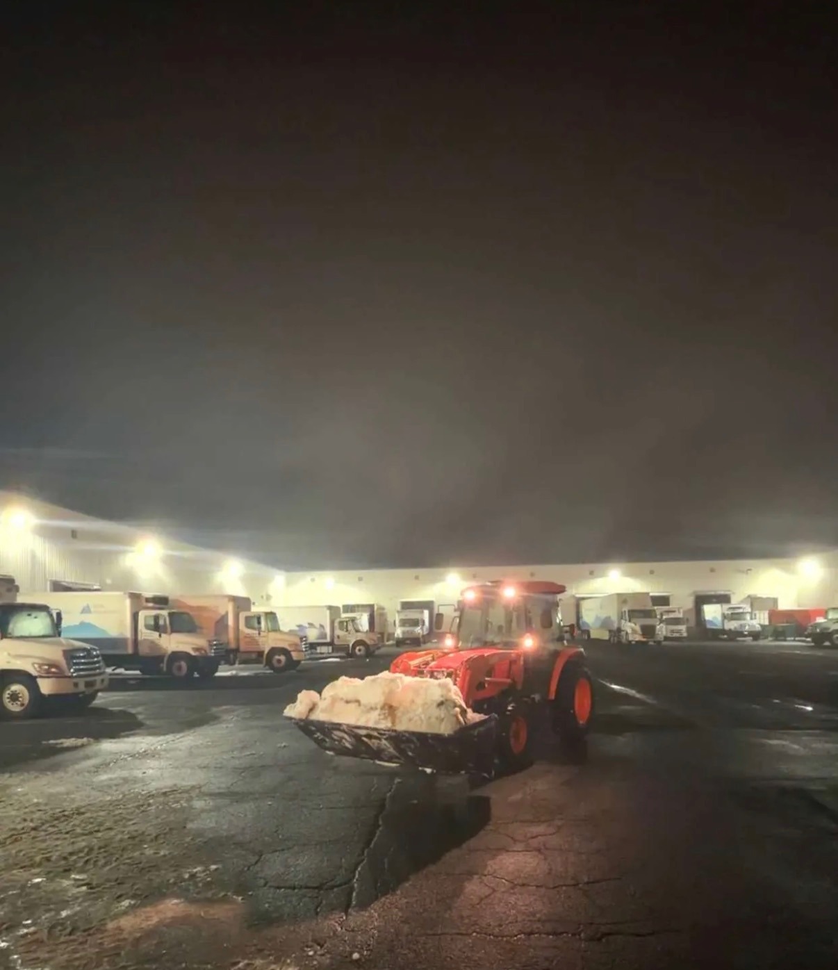 Tractor with a loaded bucket of snow at a distribution center loading dock overnight