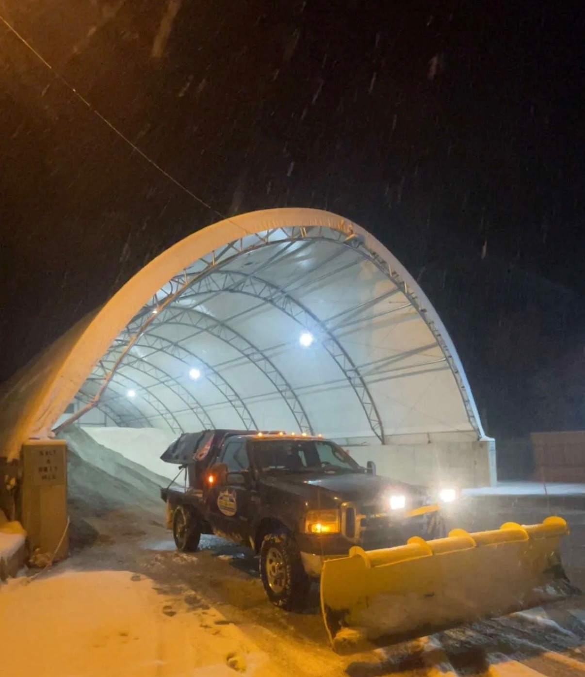 JRW Services plow truck pulling into a covered salt dome during a snowstorm at night
