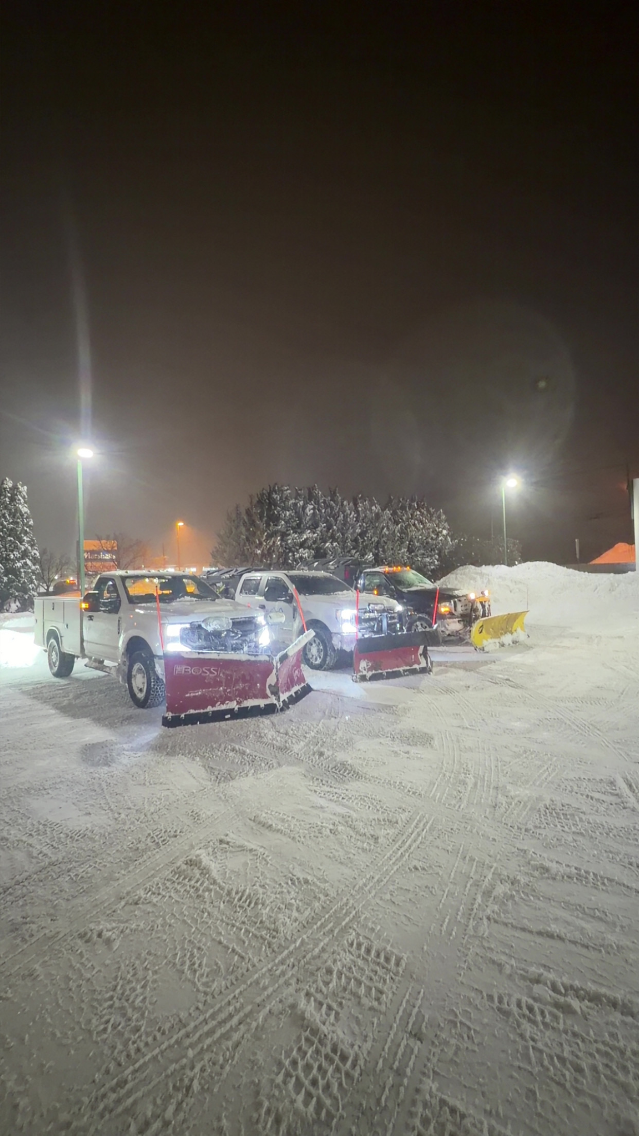Two JRW Services plow trucks staged at night with plows mounted ahead of a route